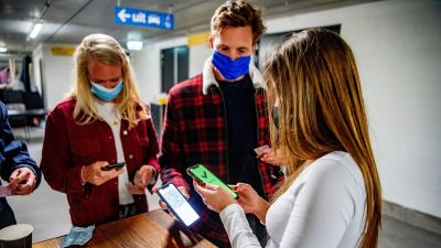 Några personer i munskydd visar telefon med coronapass på en klubb.