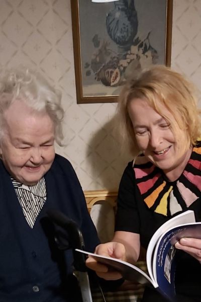 En äldre dam och en kvinna läser en bok tillsammans och ser glada ut.