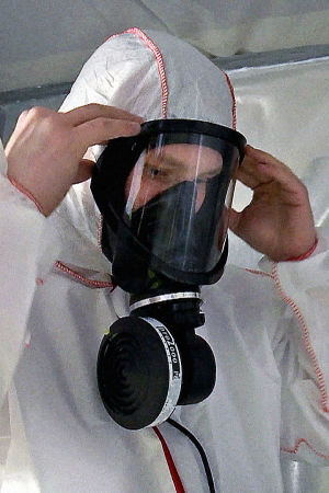Rakennustyömies pukee suojapuvun ja hengityssuojaimen asbestityömaalla.