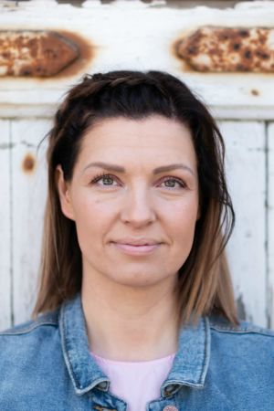 Monna Pursiainen seisoo vanhan, ruostuneen oven edessä.