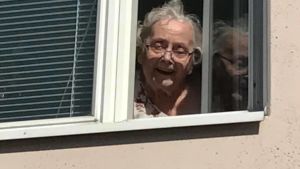 Karin Blomqvist fyller snart 94 och en stor glädje i livet är besöken från nära och kära. Kvinna som tittar ut genom fönster.