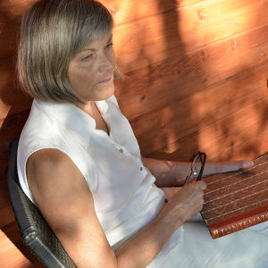Bloggaaja Marjatta Mentula istuu ilta-auringossa kädessään Tuntematon sotilas -kirja.