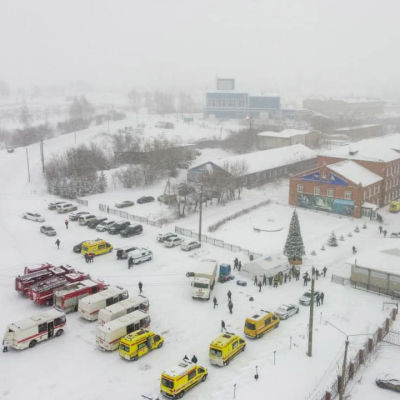 Ambulands och brandbilar står parkerade i ett snöigt landsskap bredvid flera långa tegelbyggnader