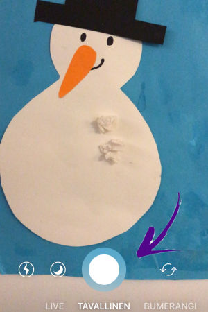 Kuvakaappaus Instagramin kamera-tominnosta. Kuvassa askarreltu lumiukko ja nuoli osoittaa IG:n kamernappia