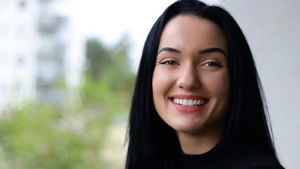 Odette är glad över att hon vågade göra en ny utredning. En kvinna med svart hår. Står ute på en balkong. Hon ler stort.