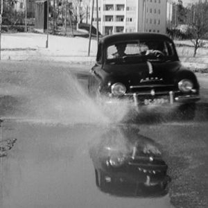 Auto roiskuttaa vettä keväisellä kadulla.