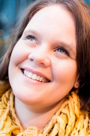 Aleksandra Mirolybov-Nurmela hymyilee kuvassa ja katsoo yläviistoon. Kuvan vasemmassa yläreunassa valkoinen Vaakakapina-leima.