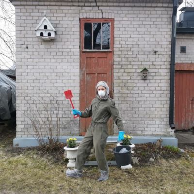 kvinna i mask och spade framför byggnad