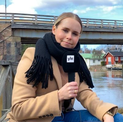 En kvinna som ler och sitter på en bänk nedanför en bro.