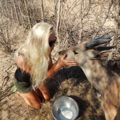 Michelle  Gustafsson i Botswana, ökenlandskap, sitter på knä och klappar en antilop