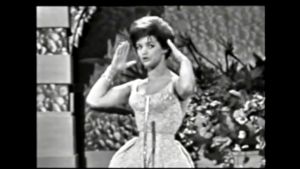Lill-Babs demonstrerar hur flickorna tar på sig sina nya hattar våren till ära. Lill-Babs tävlade för Sverige i Eurovisionen år 1961.