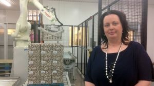 Annika Boström, VD för Boströms bageri, står bredvid en robot som lyfter lådor på plats