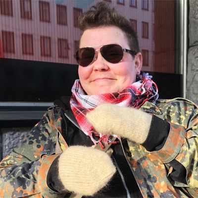 Nainen aurinkolaseissa kadulla, kädessä lapaset