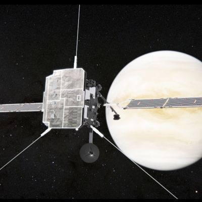 Luotain aurinkopaneelisiivet levällään tähtien täplittämässä avaruudessa, takana kellertävä Venus-planeetta.