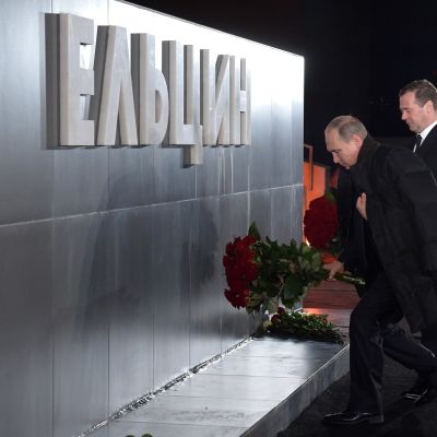 Putin ja Medvedev laskevat punaisia ruusuja metallisen seinämän eteen. Seinämässä lukee suurilla kohokirjaimilla "Jeltsin".