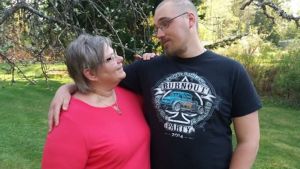 Anne Andersson med sonen Tony, Kvinna i kort grått hår och röd tröja håller om yngre man i svart t-shirt och glasögon. De står på en gräsmatta.