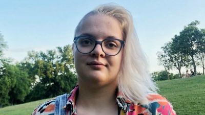 Verónica Radványi iklädd en färgglad t-shirt i en park. Hon har glasögon och silverblont hår.