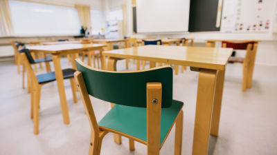 Ett tomt klassrum där stolar, pulpeter och en svart tavla syns.