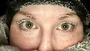 Lähikuvs naisen kasvoista, jonka ripset ovat jäätyneet pakkasessa