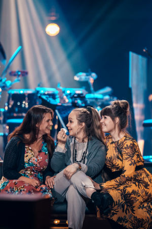 Kolme naista istuvat SuomiLOVEn lavan reunalla nauraen.