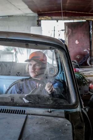 Näyttelijä Juho Uusitalo istuu autonromun ratissa sekaisessa autotallissa ja tuijottaa vakavana eteensä