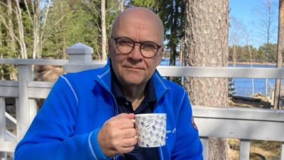 En man med en kaffemugg sitter nära havet.