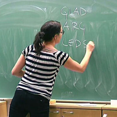 En kvinna skriver på en tavla i ett klassrum.