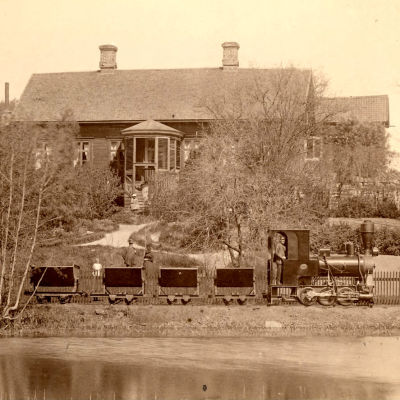 Ångloket Lill-Bässen drar kolvagnar längs Åkerraden på Fiskars bruk på 1890-talet. I bakgrunden står huset Fagerbo.