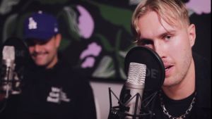 Joel Kotivuori, till höger, säger att ansiktsskydden blivit ett större modefenomen tack vare pandemin. till höger sitter joel kotivuori vid en mikrofon. han har blont hår och svarta kläder