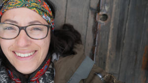 Angeliqa vågade säga upp sig för att satsa på sin riktiga dröm. En kvinna med glasögon och en scarf knuten runt huvudet. Ligger på ett träunderlag och tittar in i kameran.