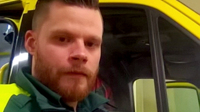 Ambulanschaufför står bredvid en ambulans.