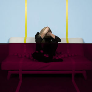 Verona-nimisen artistin promokuva, jossa hän istuu sohvalla pää painuksissa käsissä. Taustaseinä on alapuolelta tumma ja yläpuolelta kirkas.
