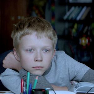 Koulupoika Aljosha (Matvei Novikov) tuijottaa ulos ikkunasta kirjoituspöytänsä ääressä elokuvassa Vailla rakkautta