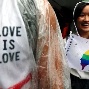 Nainen näyttää kuvaa sateenkaaren väreissä olevasta Taiwanin kartasta. Vasemmassa reunassa Love is love -teksti.