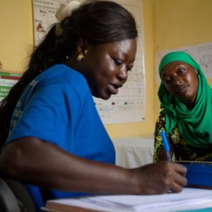 nainen klinikan vastaanotolla kuuntelee, terveydenhoitaja kirjoittaa paperiin