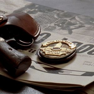 Revolveri koteloineen ja Los Angelesin poliisin virkamerkki makaavat pöydällä sanomalehden päällä. Kuva elokuvasta L.A. Confidential.