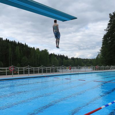 Mies hyppää hyppytornista altaaseen maauimalassa