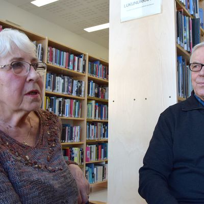 Nainen ja mies istuvat kirjastossa ja keskustelevat