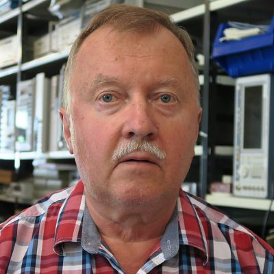 Mies lähikuvassa taustalla tietokoneita