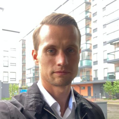 En man står utanför ett höghus, vädret ser mulet ut. Mannens min är neutral.