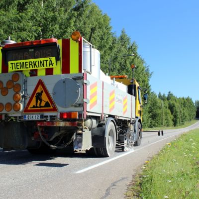 Tiemerkintäauto merkitsee maantien reunaviivaa. Auton perässä on huomiokylttejä.