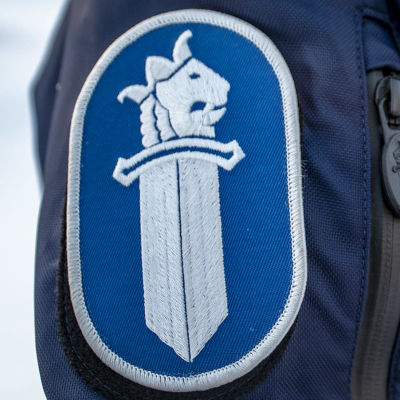 Närbild av polis i uniform. Texten poliisi polis syns på bröstet och på överarmen finns polisens emblem bestående av ett svärd och ett krönt  lejonhuvud.
