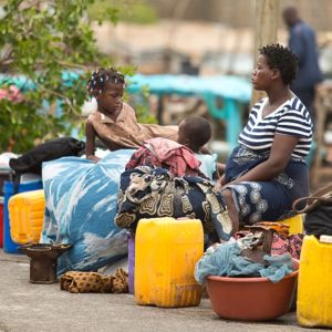En kvinna och två barn som sitter vid en väg och väntar på hjälp efter stormen Idai i Moçambique.