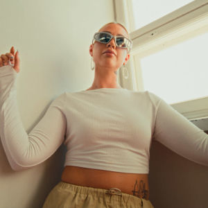 Tyyli on fresh -dokumenttisarjan päähenkilö poseeraa aurinkolaiseissa ja vaaleissa vaatteissa seinää vasten.