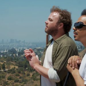 Brian Bushway ja Sean Ricks seisovat kukkulalla ja kuuntelevat maisemaa taputtamalla käsiään yhteen. Taustalla on Los Angelesin kaupunki.