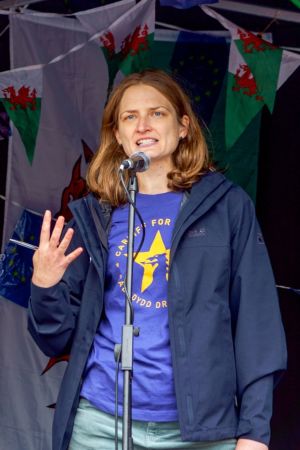Helen Wales är ledaren för en rörelse som vill att Wales stannar i EU. En person (Helen Wales) står på scen och talar i mikrofon. Wales flagga syns i bakgrunden som girlanger i bakgrunden.