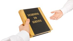 Käsi ojentaa kirjaa toiselle kädelle. Kirjan kannessa lukee: Learning to Survive.