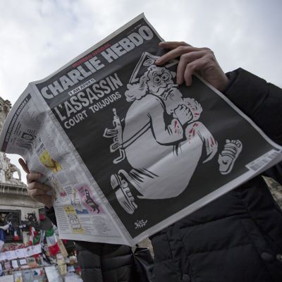 Ranskalaisesen Charlie Hebdo -lehden keskiviikkona ilmeestyneen erikoisnumeron kannessa on esitettynä Jumala, jolla on verta käsissä ja rynnäkkökivääri selässä.