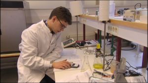 Sampo Latvakangas i färd med sina laboratorieuppgifter. En ung man i vit laboratorierock sitter med räknemaskin.