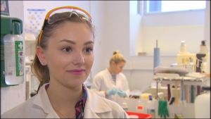 Krista Alasalmi tänker specialisera sig på livsmedelskemi. Närbild på ung kvinna i vit laboratorierock och med skyddsglasögon på huvudet.